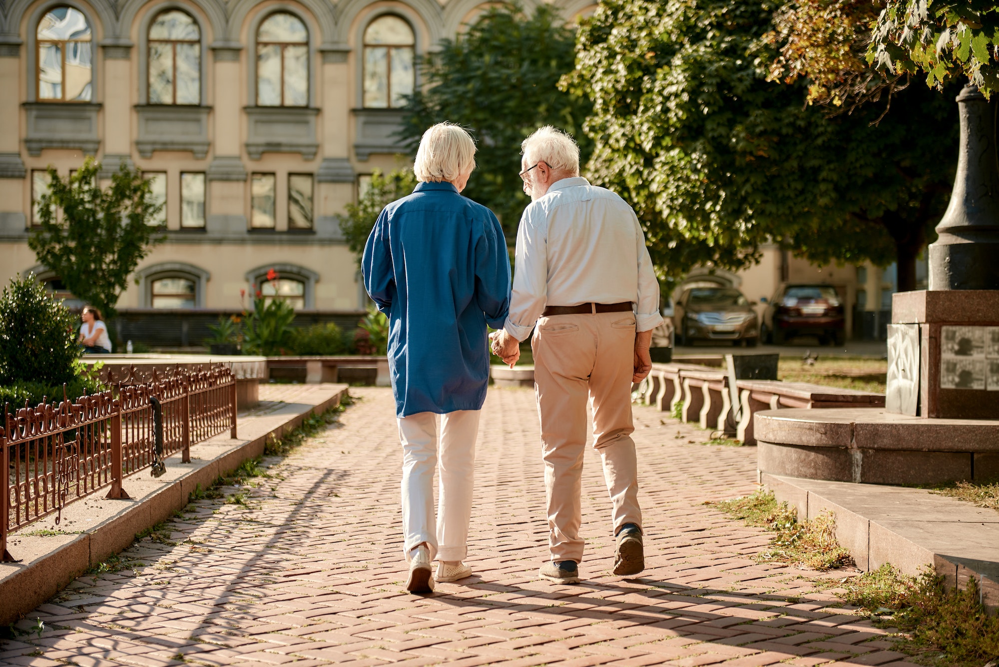 Back view of elderly couple holding hands while walking together outdoors